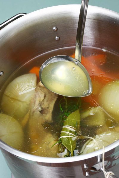 Homemade chicken stock ingredients in a stockpot with a ladle