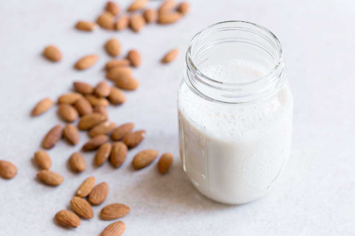 raw almonds scattered on counter for an almond milk recipe, and jar of nut milk next to them