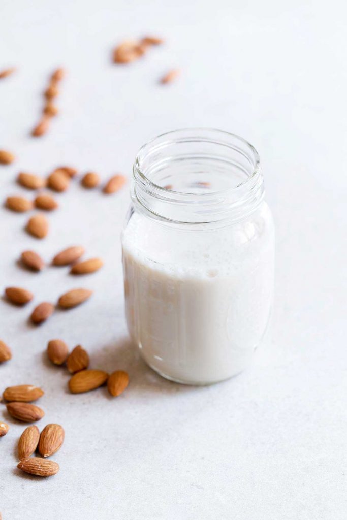 Homemade almond milk stored in a glass mason jar, surrounded by raw almonds