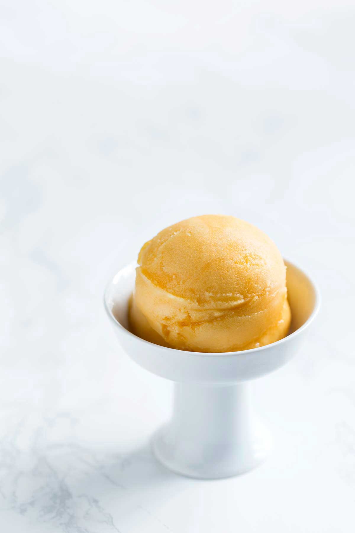 Passion fruit sorbet in a white bowl on a marble backdrop. 