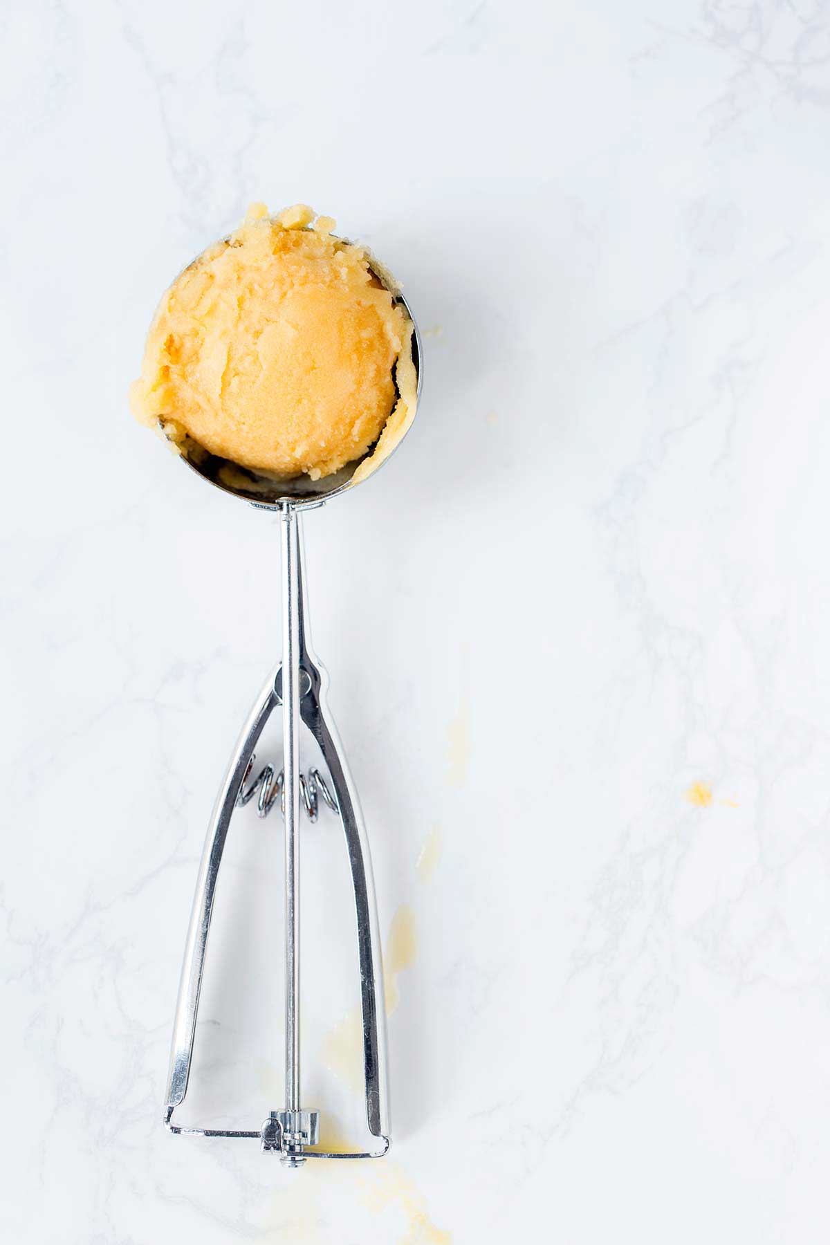 A scoop of passion fruit sorbet on a marble backdrop