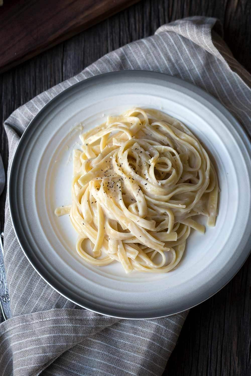 Fettuccine with Vegan Alfredo Sauce on white and grey plate, shot from overhead.