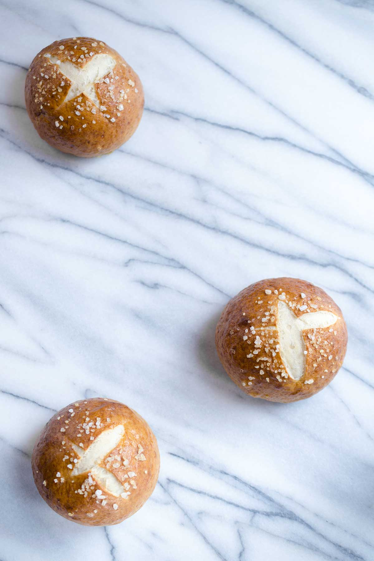 Three pretzel rolls on a marble backdrop.