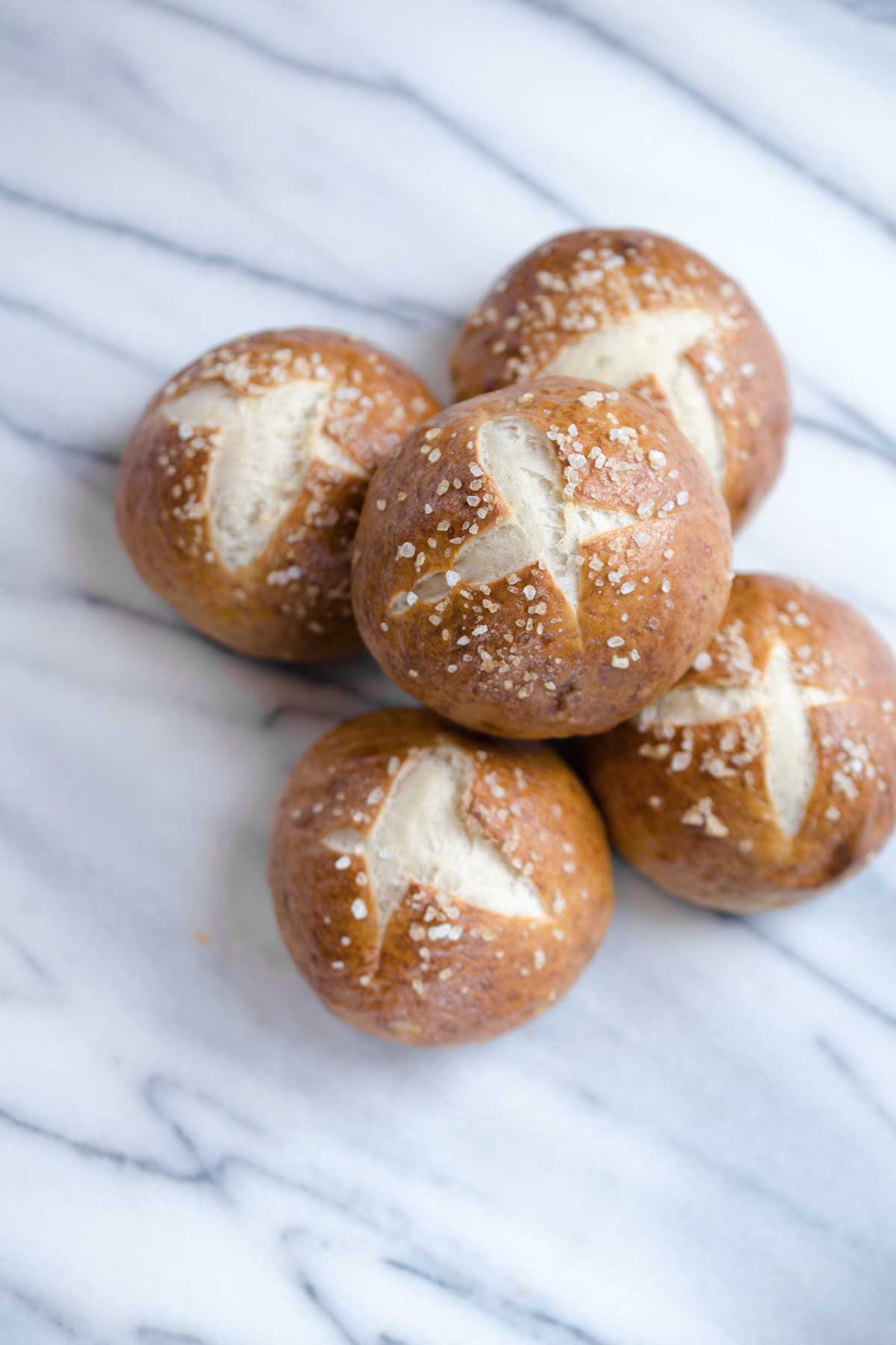 An overhead photo of 5 pretzel buns topped with coarse salt on a marble backdrop.