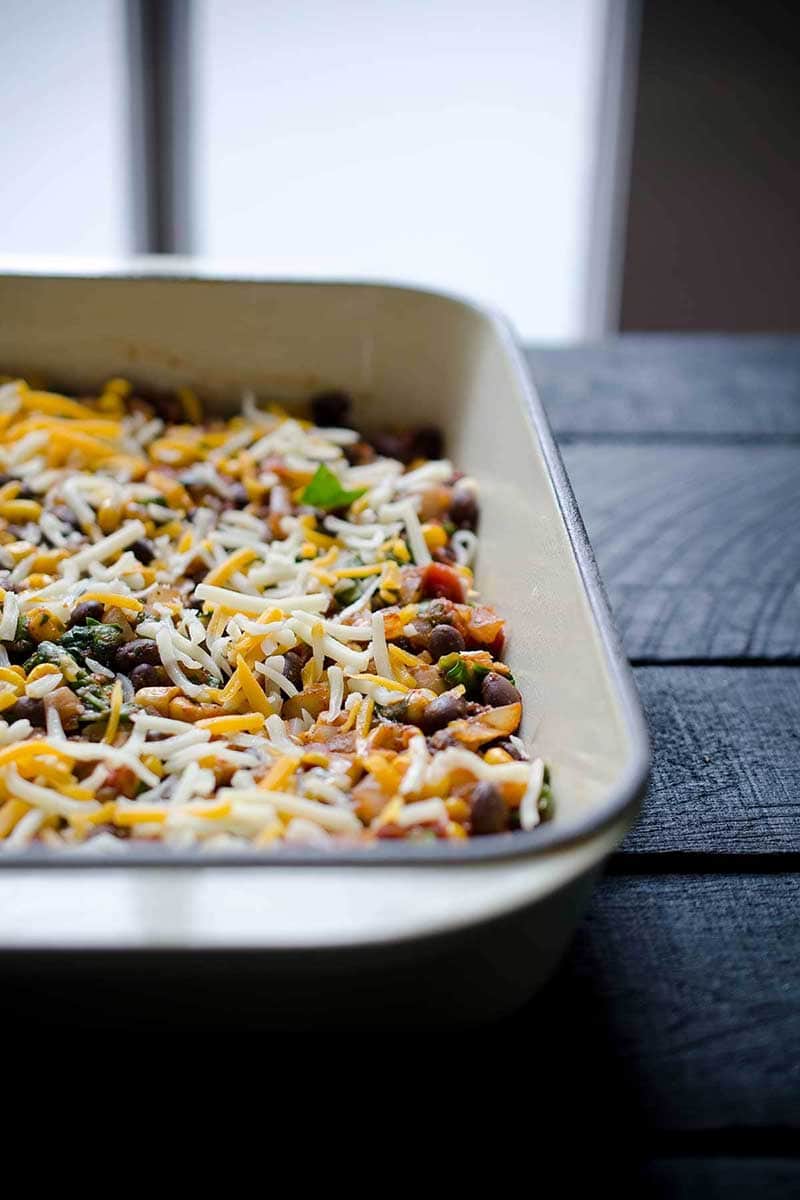 taco bake with tortillas partially filled up the dish, mid-layering.