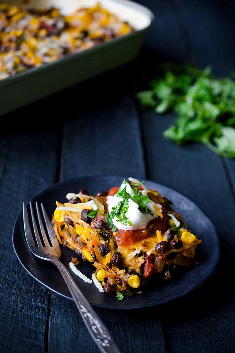 A slice of Mexican casserole on a plate, topped with sour cream and cilantro.
