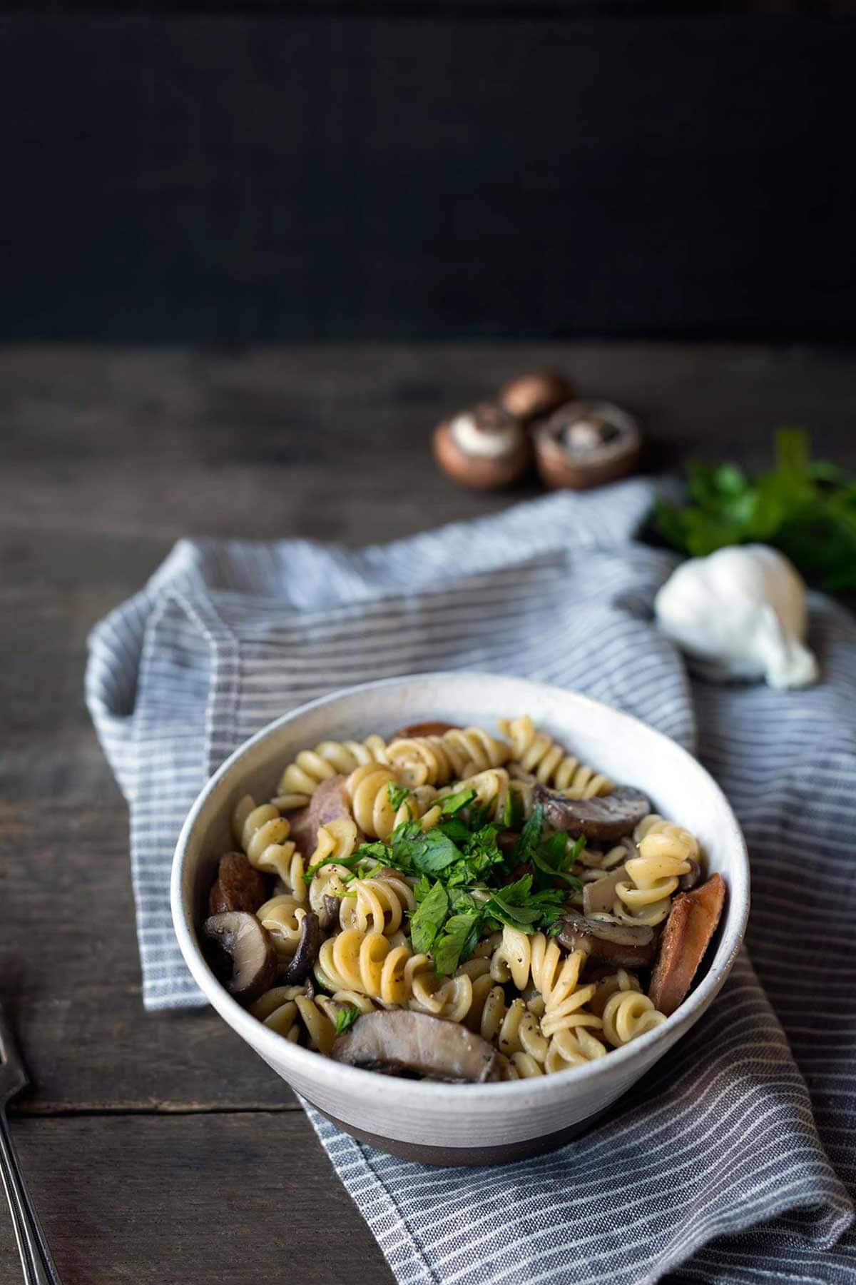 Closeup of mushroom pasta topped with parsley, surrounded by mushrooms and garlic.