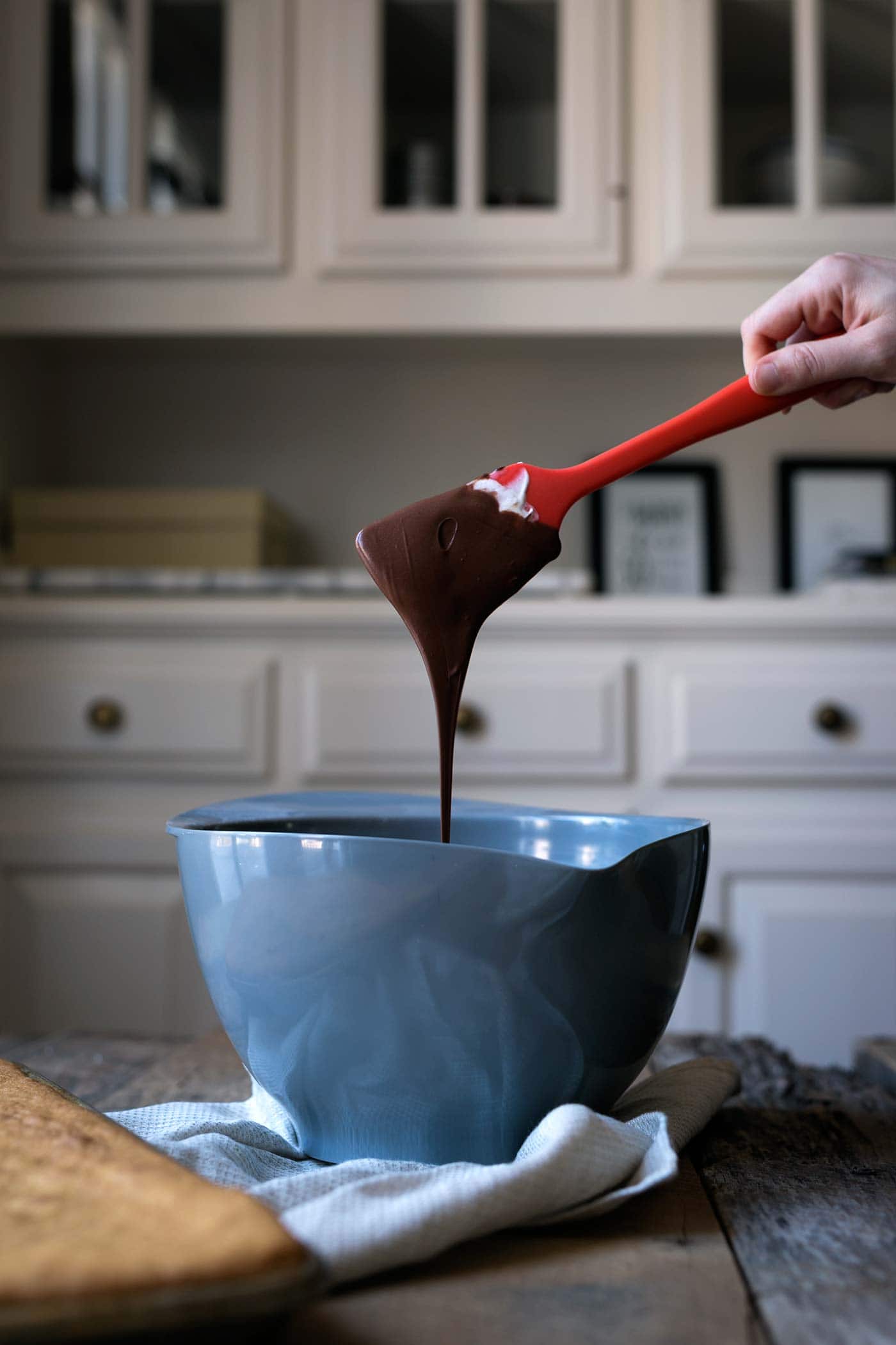 Melted chocolate dripping from a spatula into a bowl