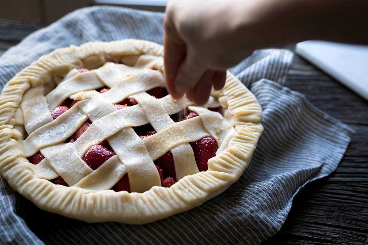 A hand sprinkling coarse sugar over raw pie dough.
