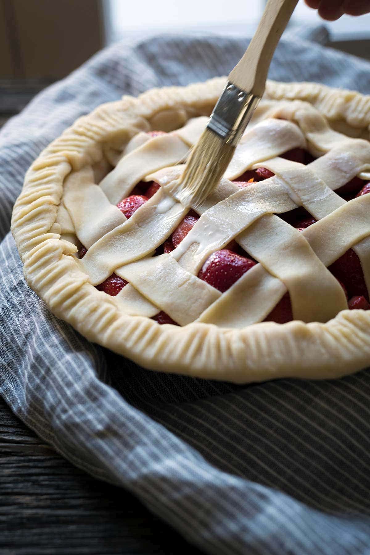 Brushing cream onto pie dough before baking to help brown up the crust in the oven.