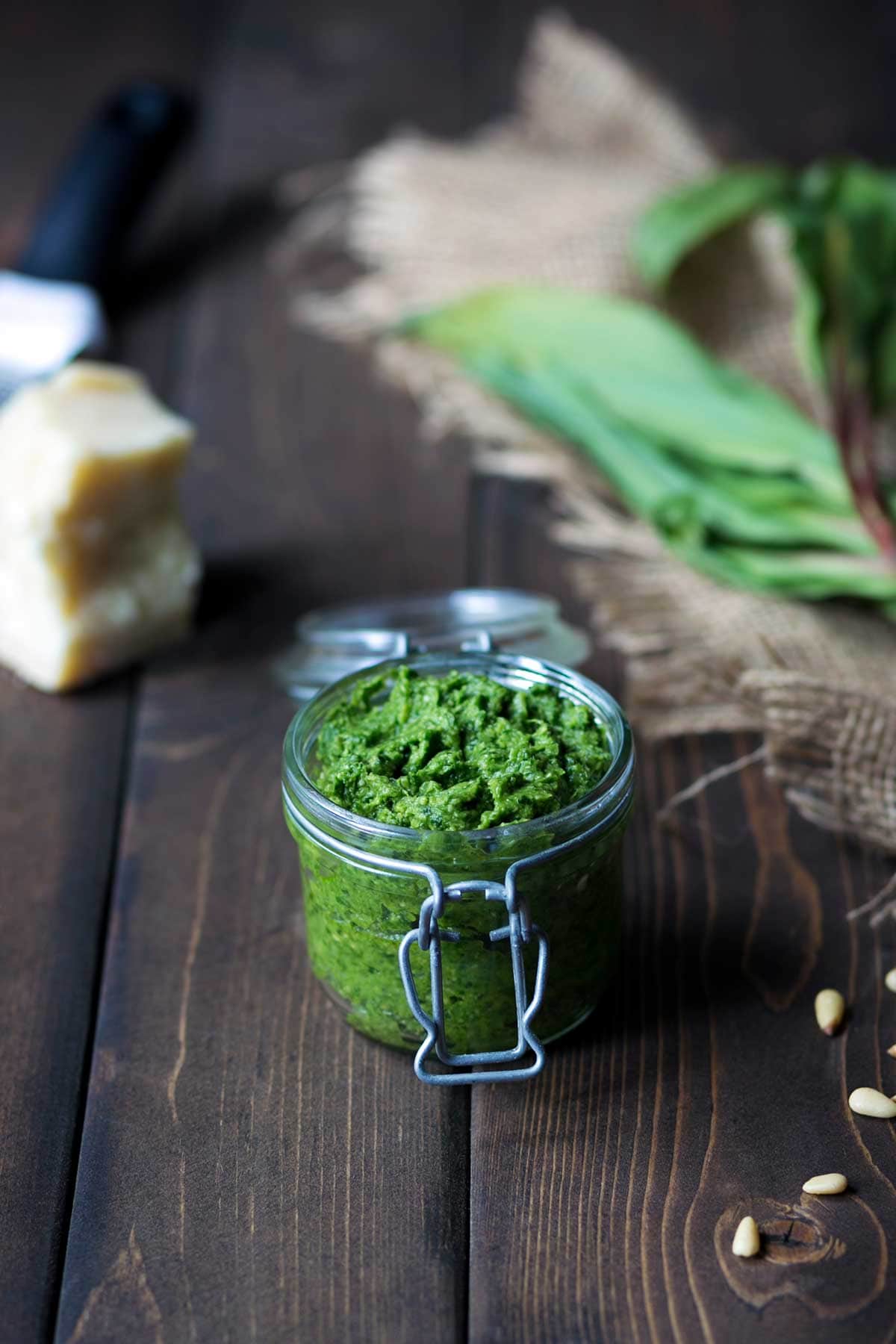 Ramp pesto recipe in a mason jar, surrounded by pesto ingredients including parmesan cheese, pine nuts, and ramps.