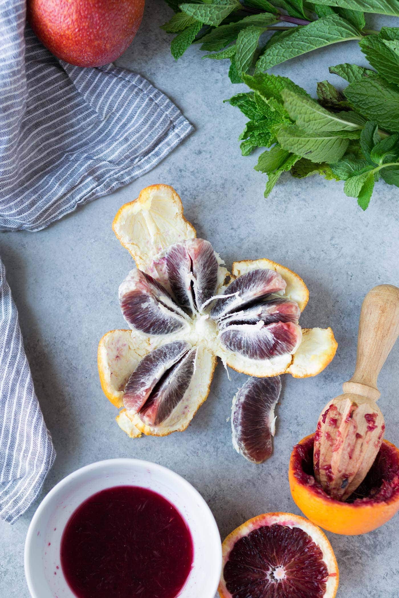 blood orange segments next to wooden citrus juicer and small dish of blood orange juice