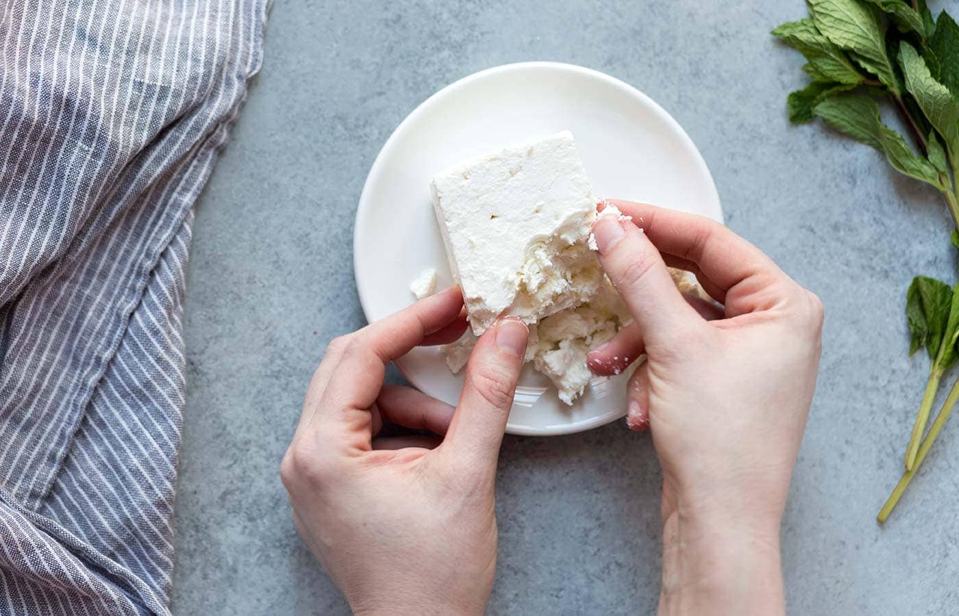 woman's hands crumbling block of feta cheese on small white plate