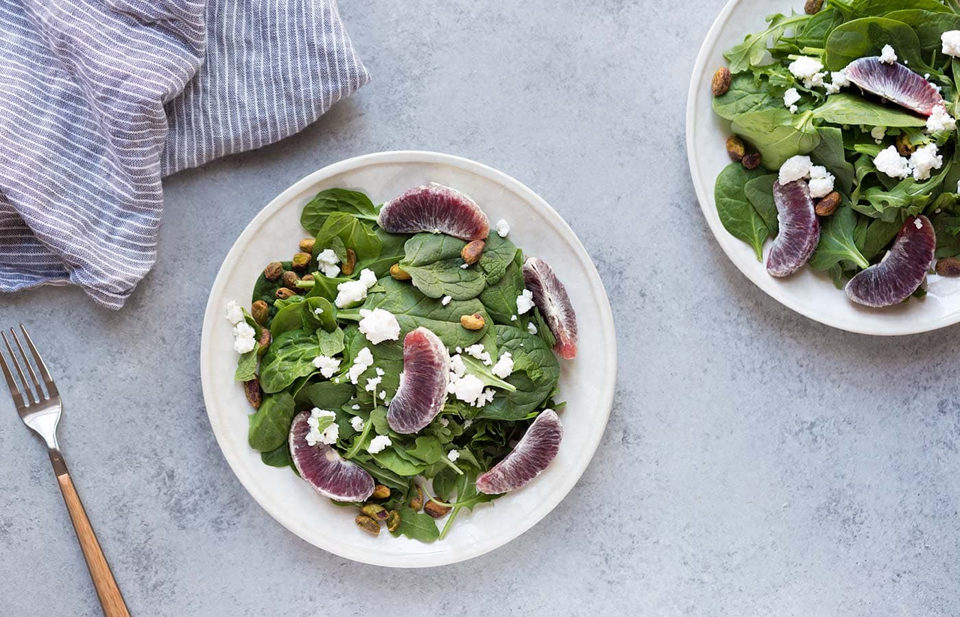 spinach and arugula on plates with blood orange slices pistachios and feta cheese