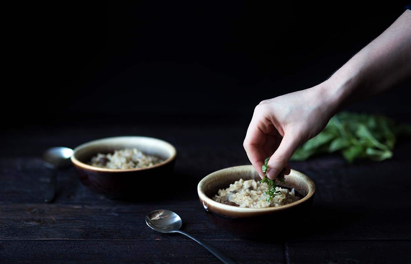 hand sprinkling fresh basil over bowls of savory oatmeal