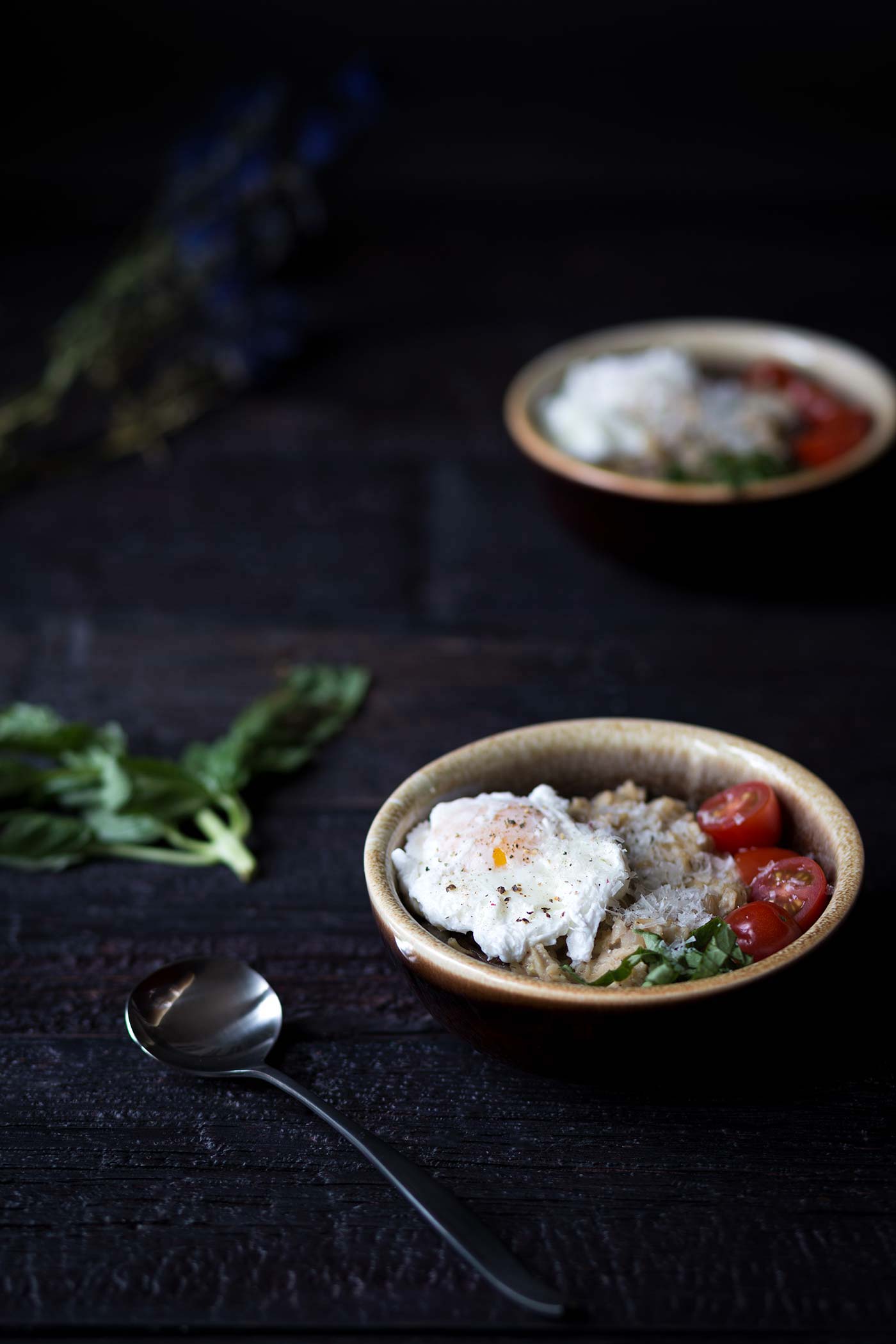 bowls of savory oatmeal with egg and tomatoes on a dark background