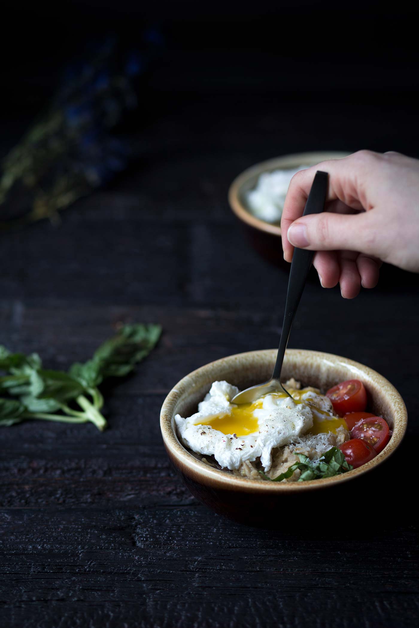 inserting a spoon into mushroom oatmeal and eggs with basil and sliced tomatoes