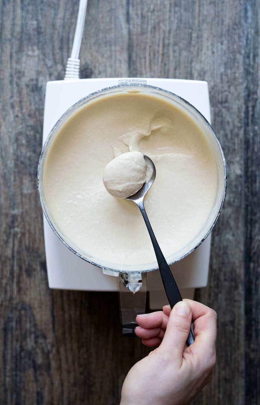 A close up photo of homemade hummus in a food processor, scooped with a spoon.