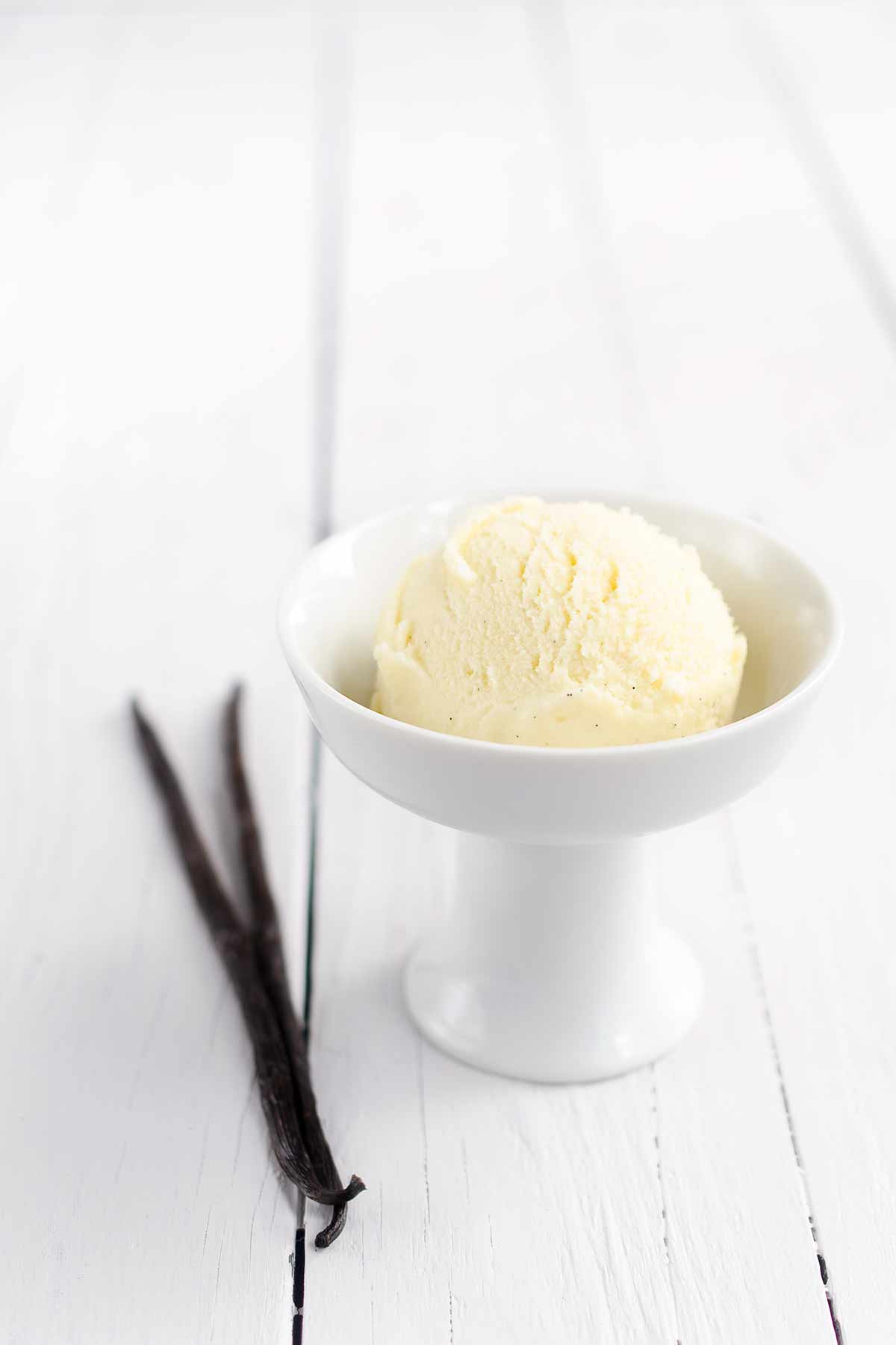 Vanilla milk gelato in a white bowl next to a vanilla bean.