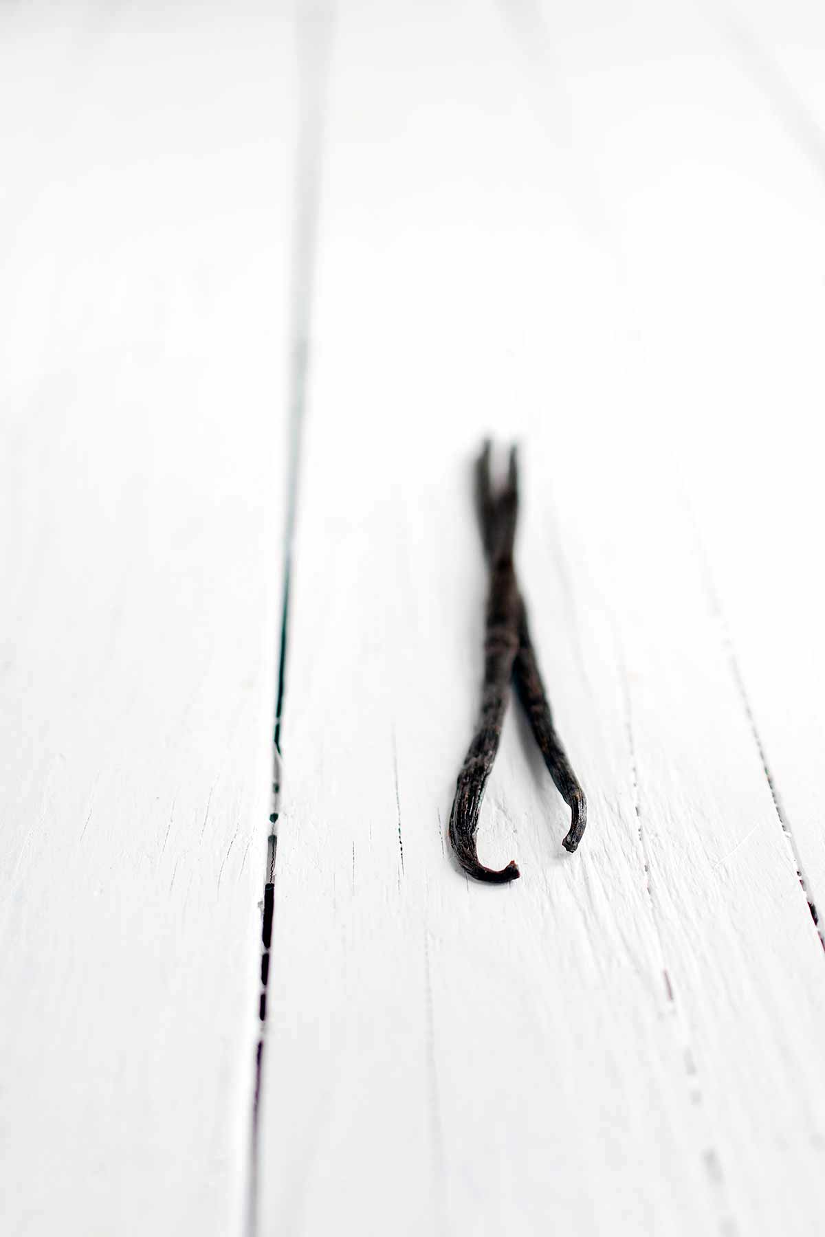 Two vanilla beans on a white backdrop.