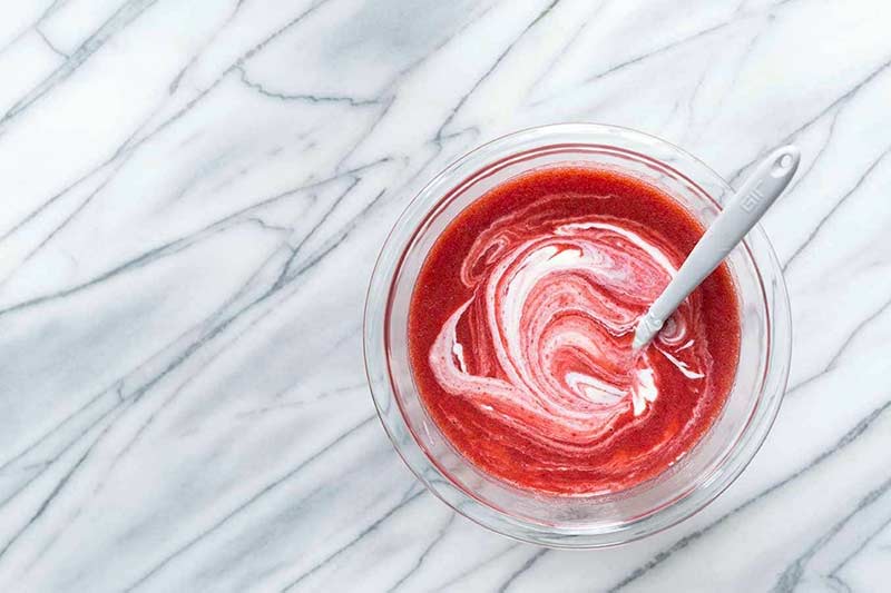 spoon in a bowl of strawberry puree swirled with yogurt on gray marble background