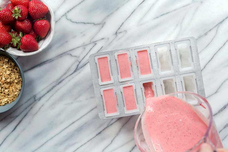 pouring strawberry mixture into popsicle molds for a frozen yogurt popsicles recipe