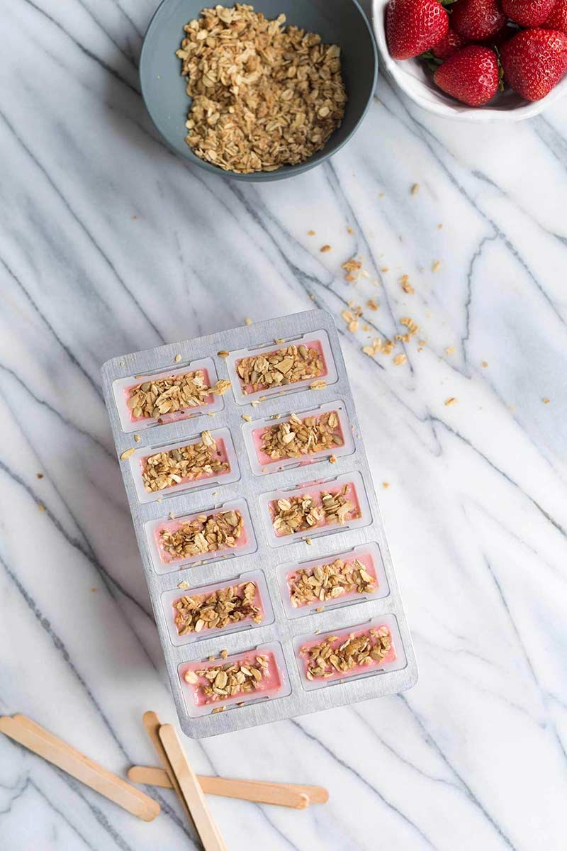 overhead image of granola on top of strawberry popsicles in molds