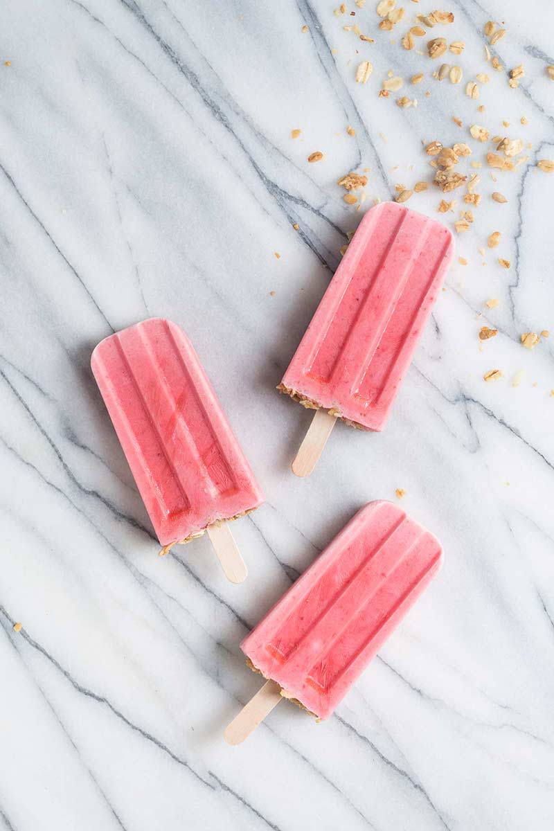 strawberry yogurt popsicles with granola on wooden sticks