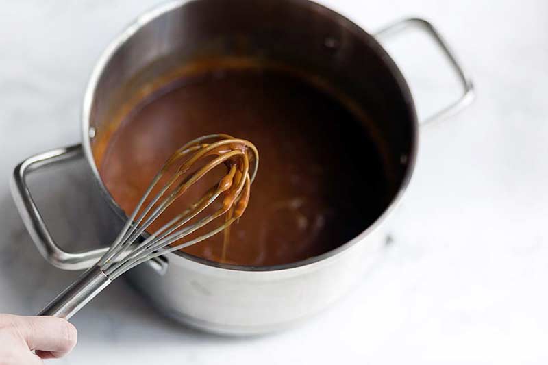 A photo of a whisk dipped into a sauce pot of salted caramel.