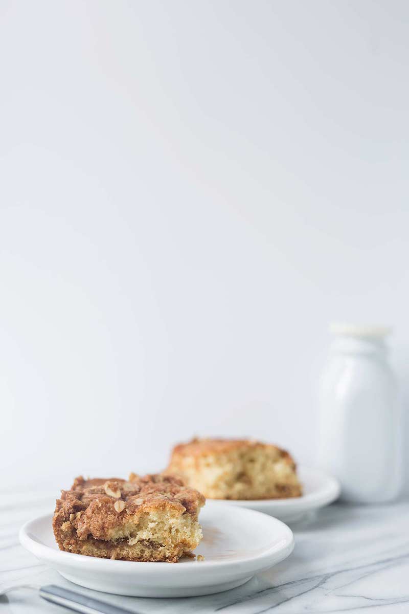 side view: 2 servings of cinnamon streusel coffee cake on white plates with bottle of milk in background