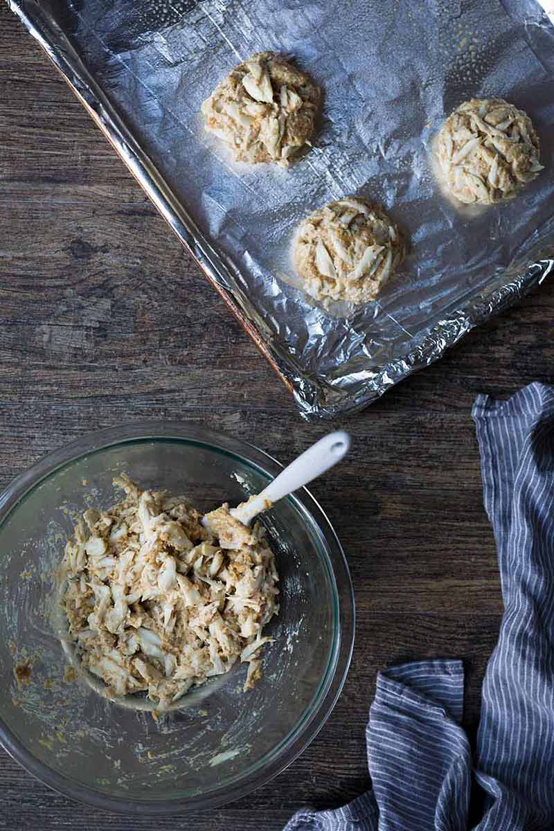 A bowl of crab cake mixture next to a sheet pan with formed crab cakes.