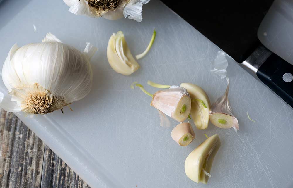 A photo of garlic sprouts, a head of garlic, and a chef's knife.