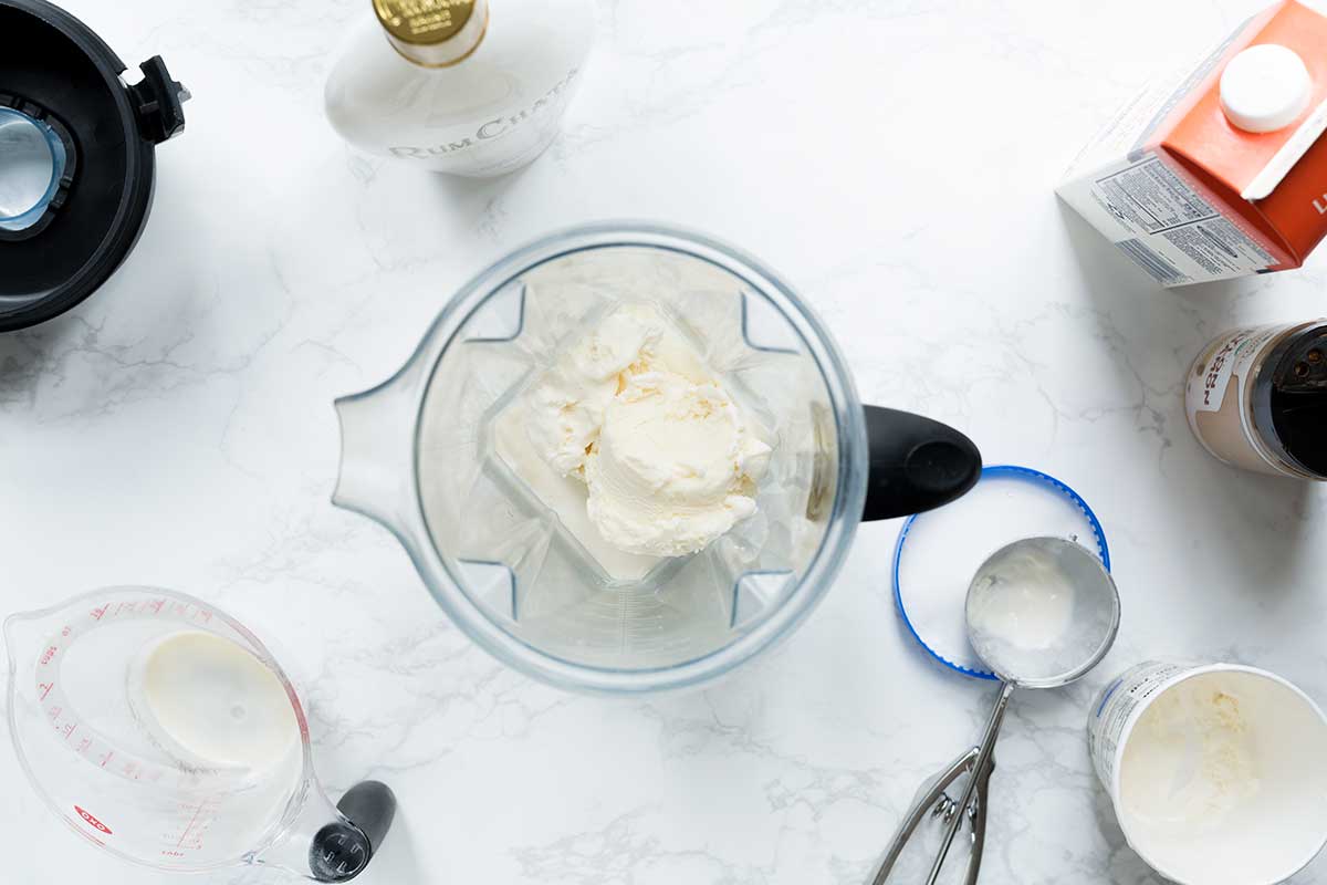 Overhead shot of a blender with RumChata drink recipe ingredients, including ice cream, cream, and cinnamon.