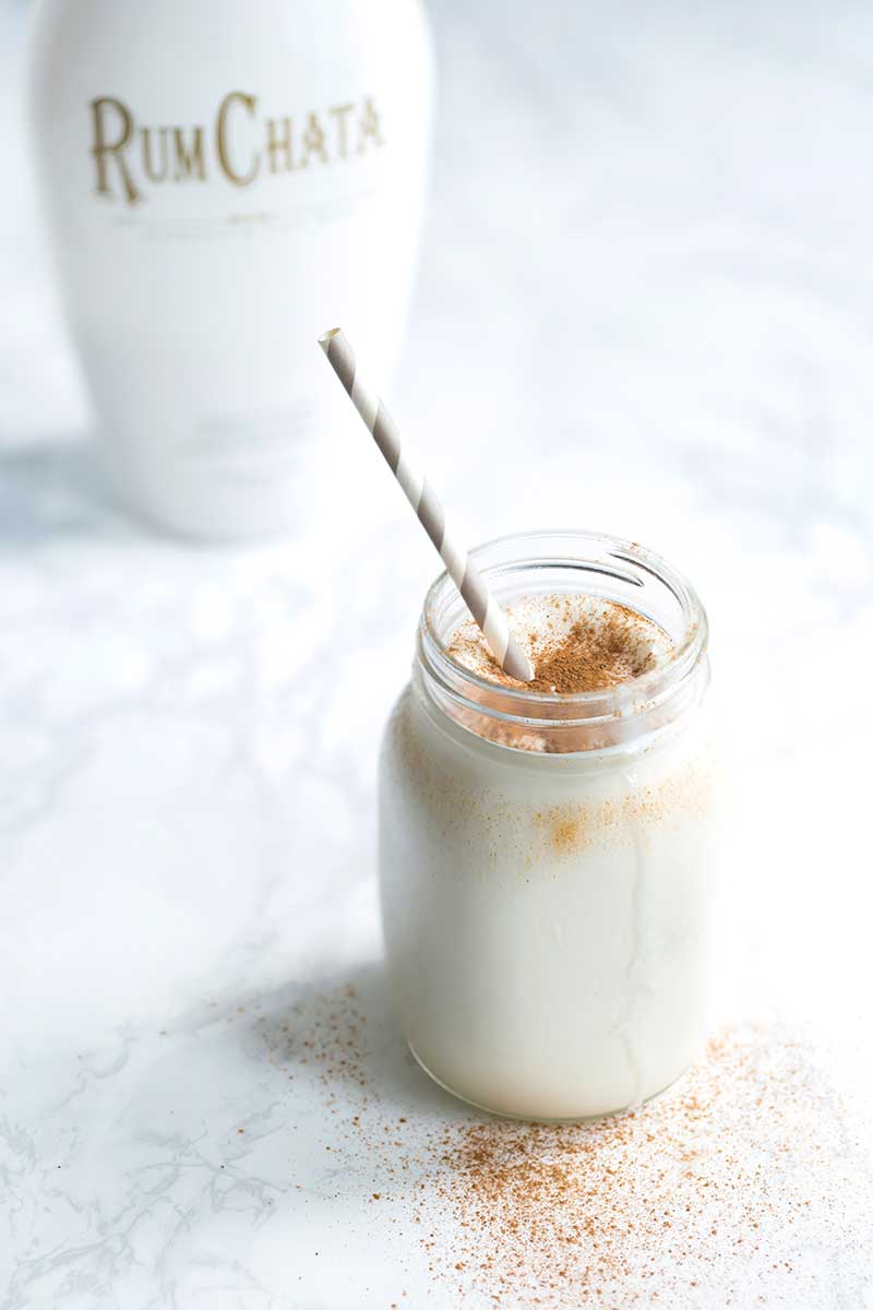 RumChata milkshake in a mason jar with a grey straw in the foreground. A bottle of RumChata in the background.