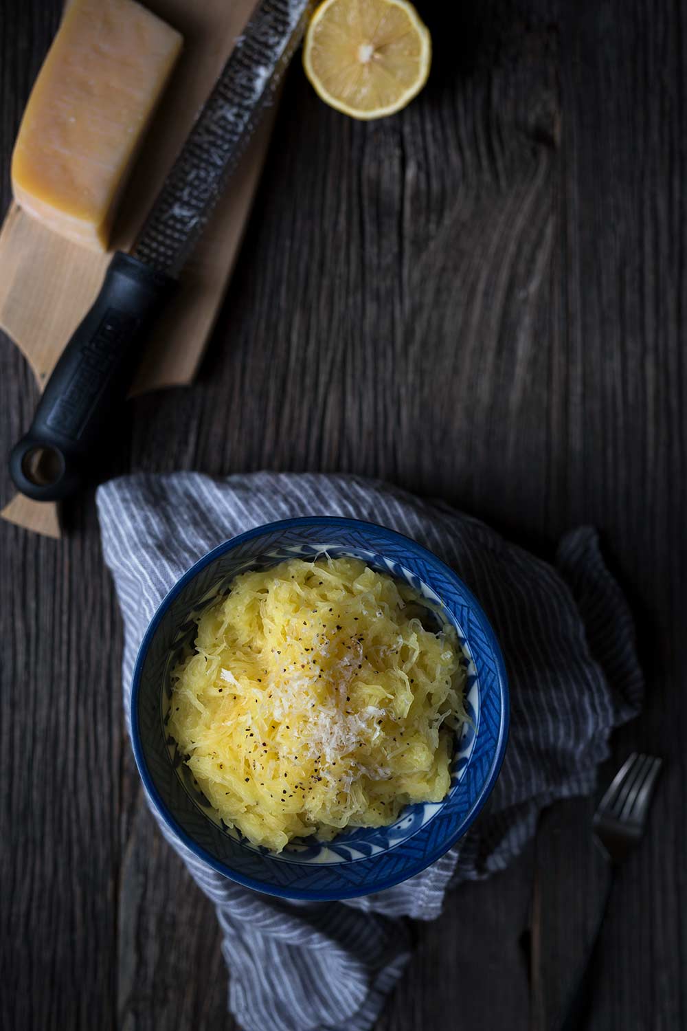 A bowl of Baked Spaghetti Squash with Butter, Parmesan, and Lemon, alongside a block of cheese and half a lemon.