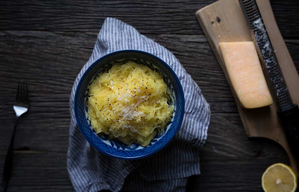 A photo of Baked Spaghetti Squash with Butter, Parmesan, and Lemon, garnished with additional grated cheese and black pepper.