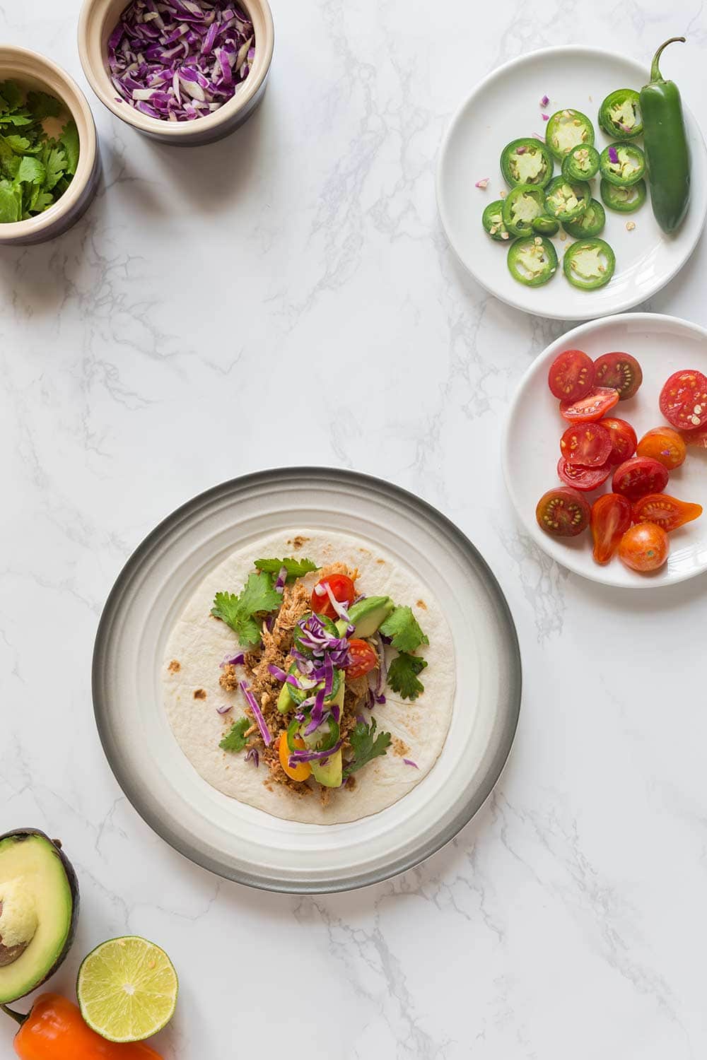 Rotisserie chicken tacos on a plate, surrounded by fixings.