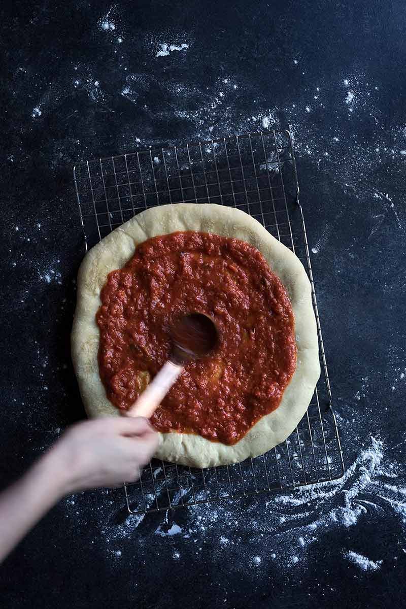 A photo of homemade frozen pizza dough being topped with pizza sauce. 