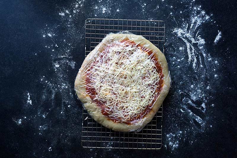 A photo of homemade pizza wrapped firmly within several layers of plastic wrap.