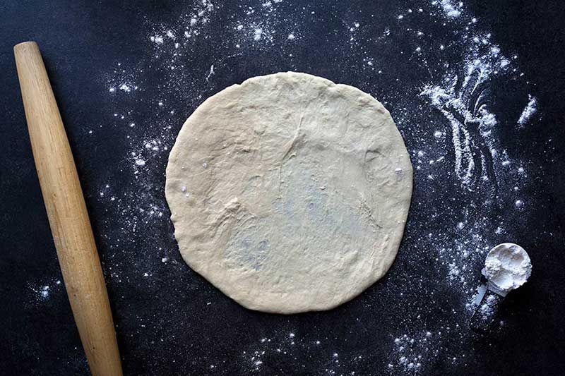 A photo of raw, homemade pizza dough, rolled out and ready to bake.