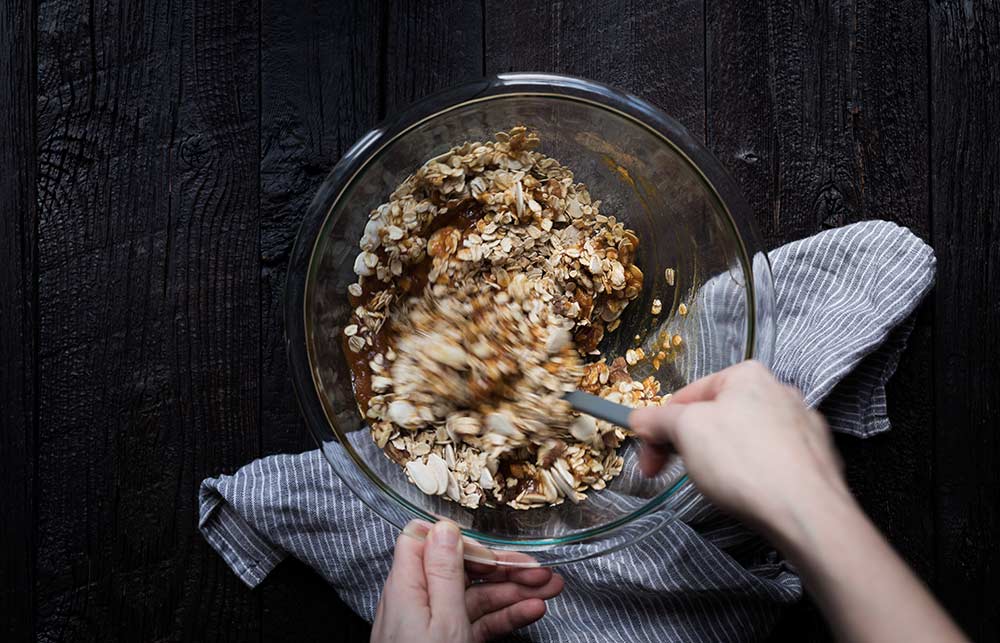 An action shot of granola ingredients being stirred together in a bowl.