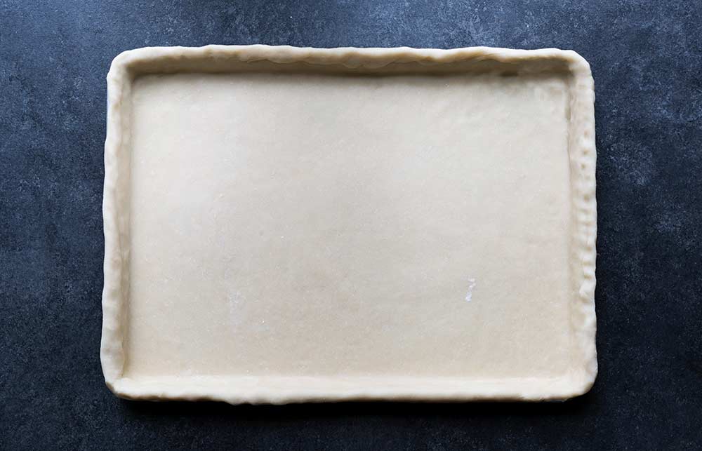A photo of unbaked pie dough rolled into a sheet pan.