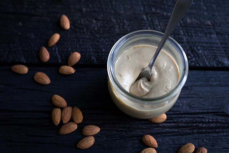 Almond butter recipe in a jar, surrounded by roasted almonds.