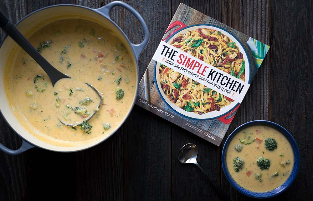 A photo of cheddar broccoli soup is a dutch oven, a bowl, and a photo of the cookbook from which the recipe originated, The Simple Kitchen.