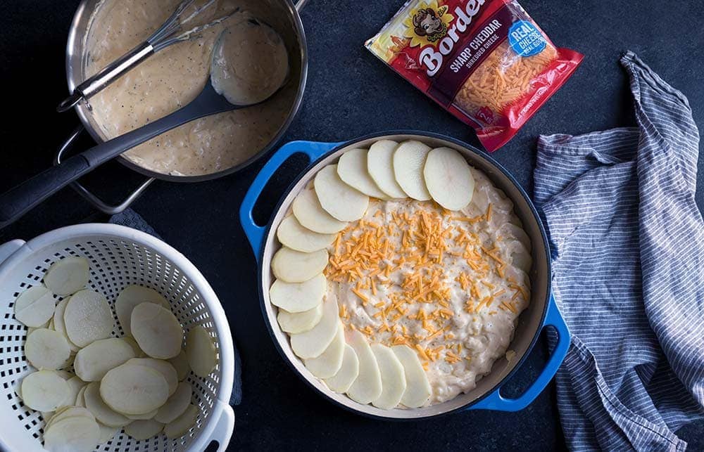 A photo of cheese and potatoes being layered into a casserole dish for au gratin potatoes.