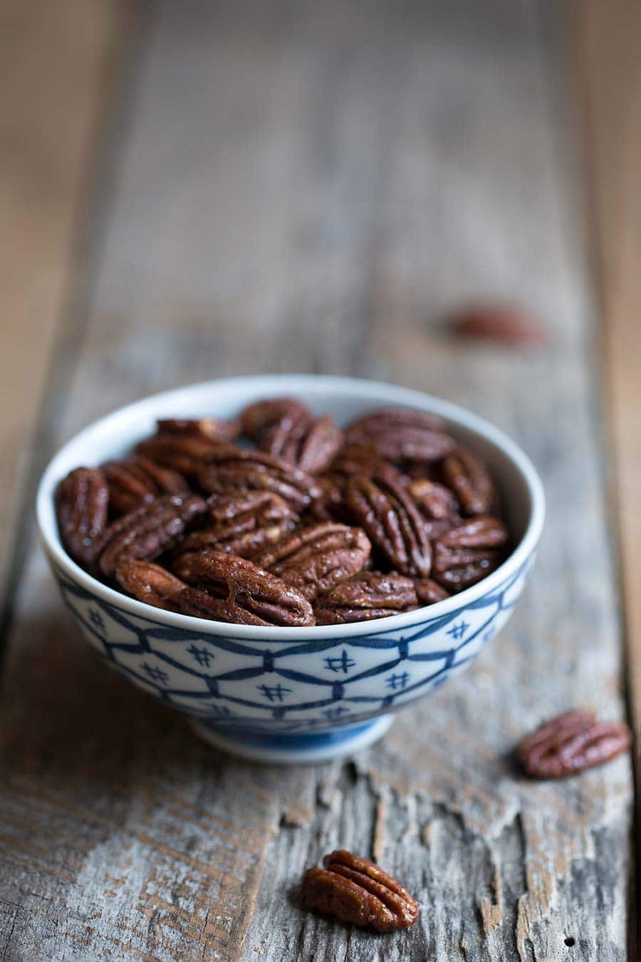 Candied pecans in a small blue and white bowl on a wood backdrop.