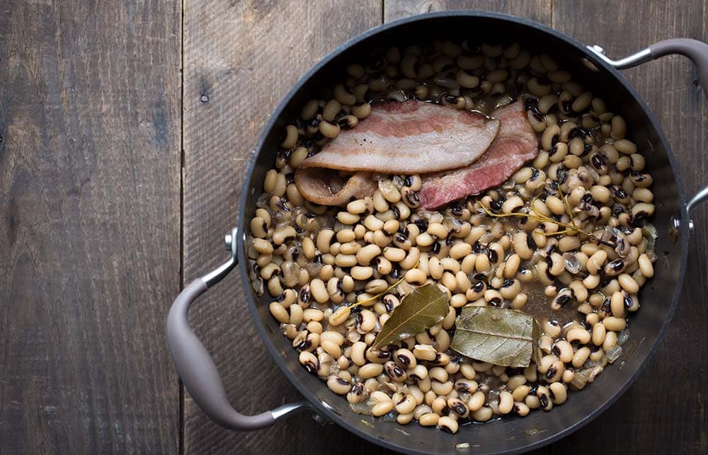 A photo of a pot of black eyed peas cooking with herbs and a slice of bacon
