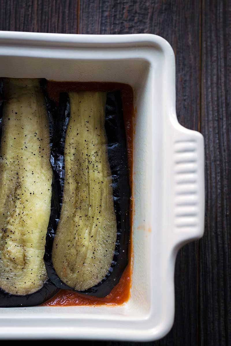 A photo of sliced, roasted eggplant being layered in a casserole dish.