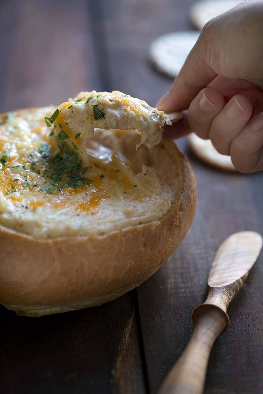 A photo of crab dip being scooped with a cracker and cheese oozing off the side.