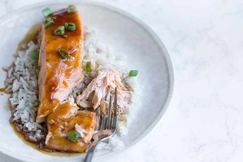 baked teriyaki salmon on a plate with white rice and a fork